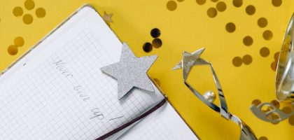 Flat lay of a notebook with motivational text, trophy, and star confetti on a yellow background.