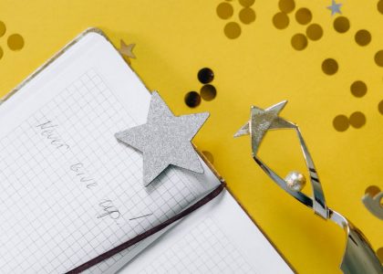 Flat lay of a notebook with motivational text, trophy, and star confetti on a yellow background.